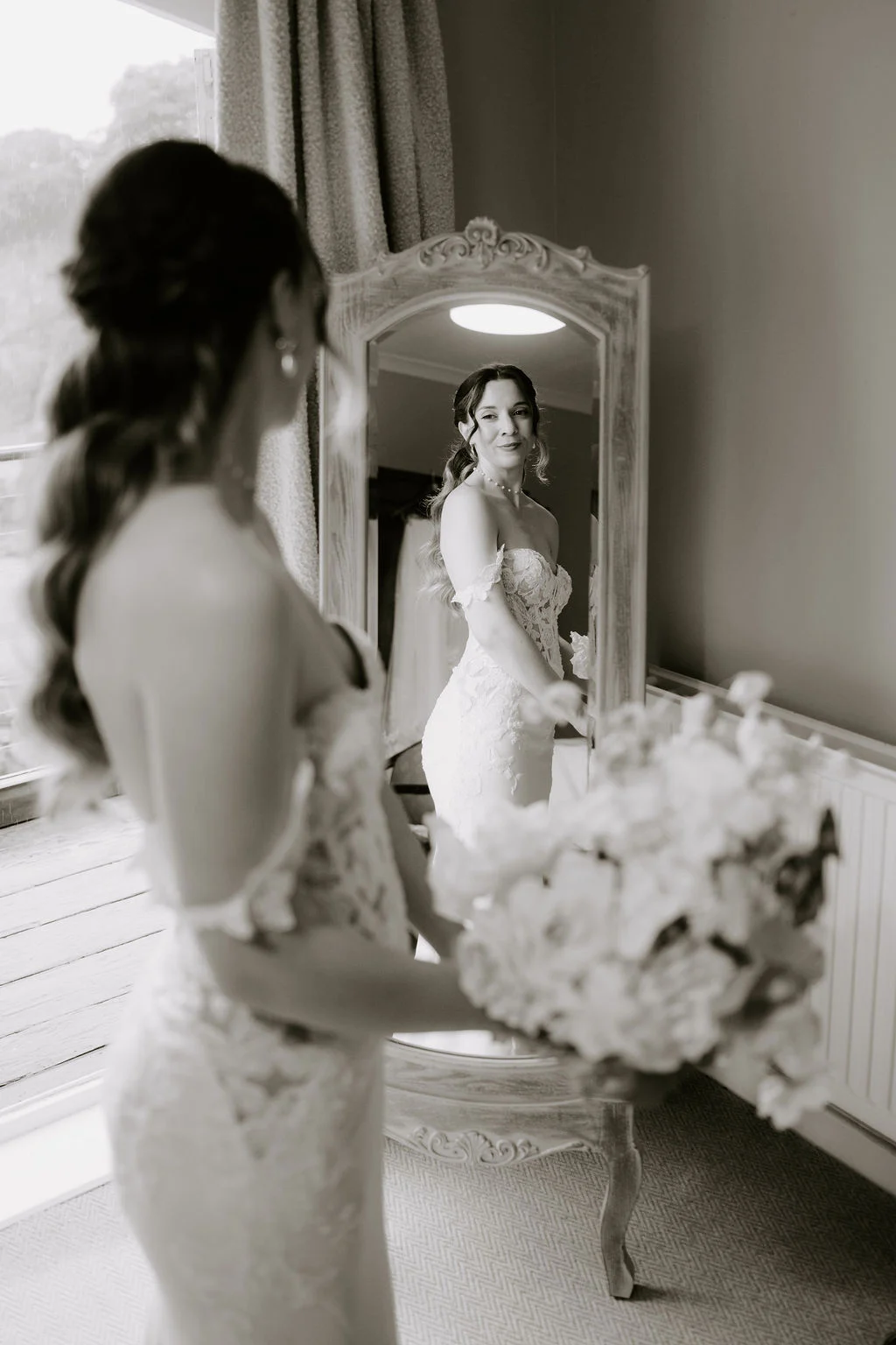Black and white photograph of Alicia beside a mirror in her wedding dress