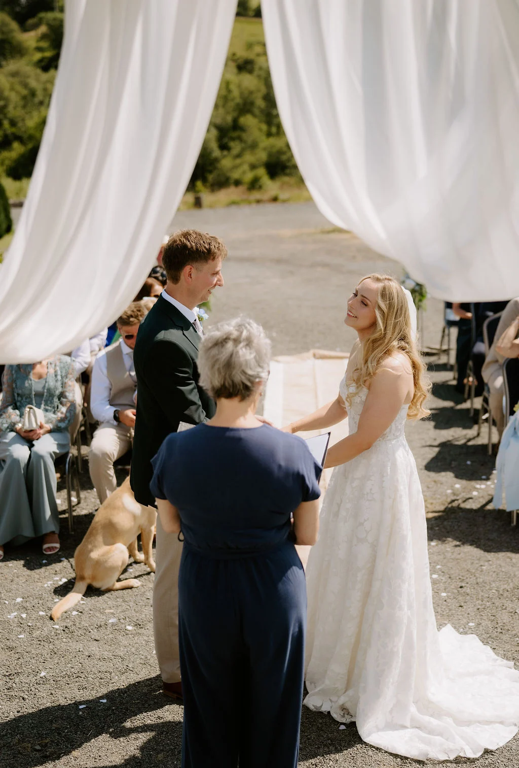 Ella and Josh exchanging vows beneath a white-draped outdoor ceremony arch
