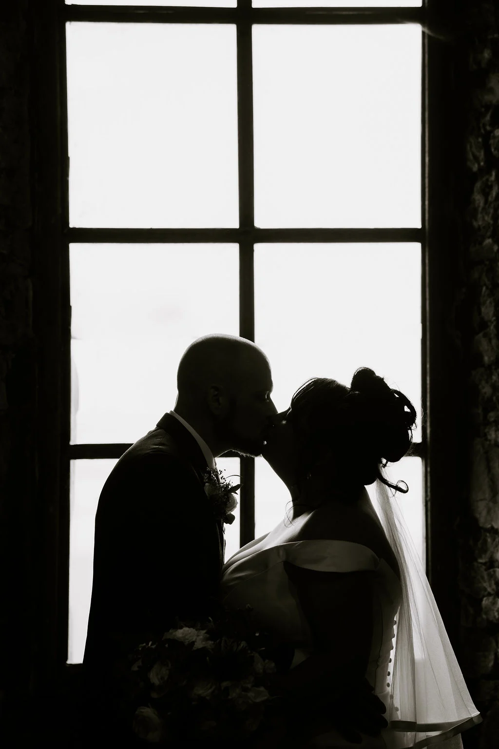 Silhouette of Jen and Nick kissing beside a large window