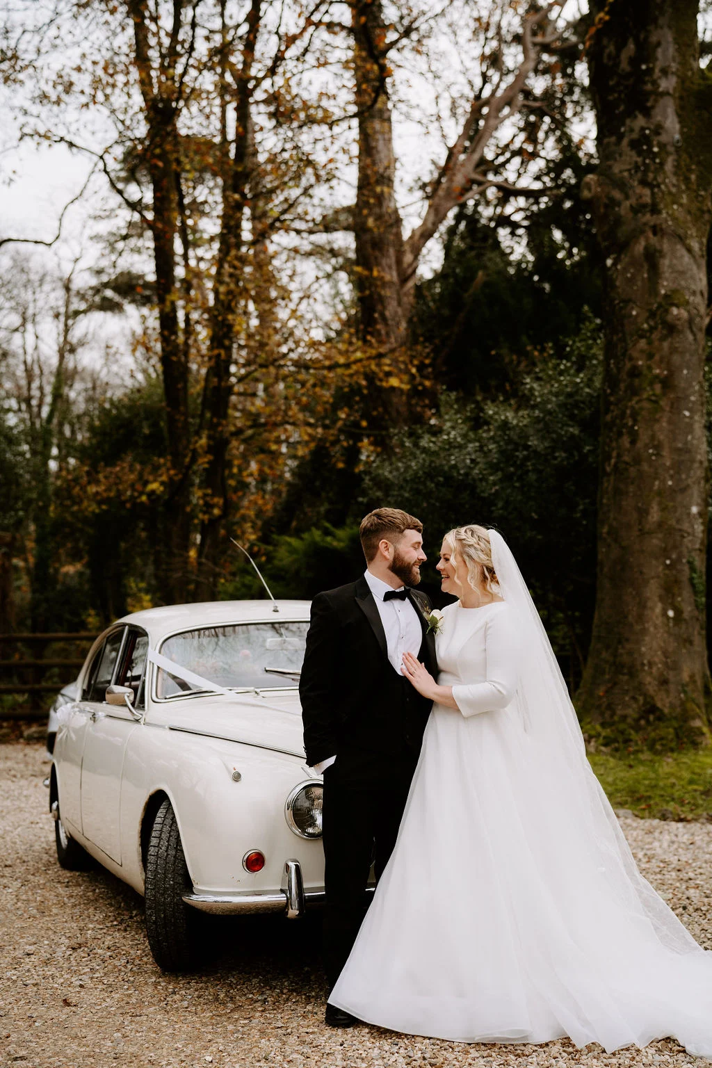 Max and Gwen standing beside a camper van on a tree-lined drive