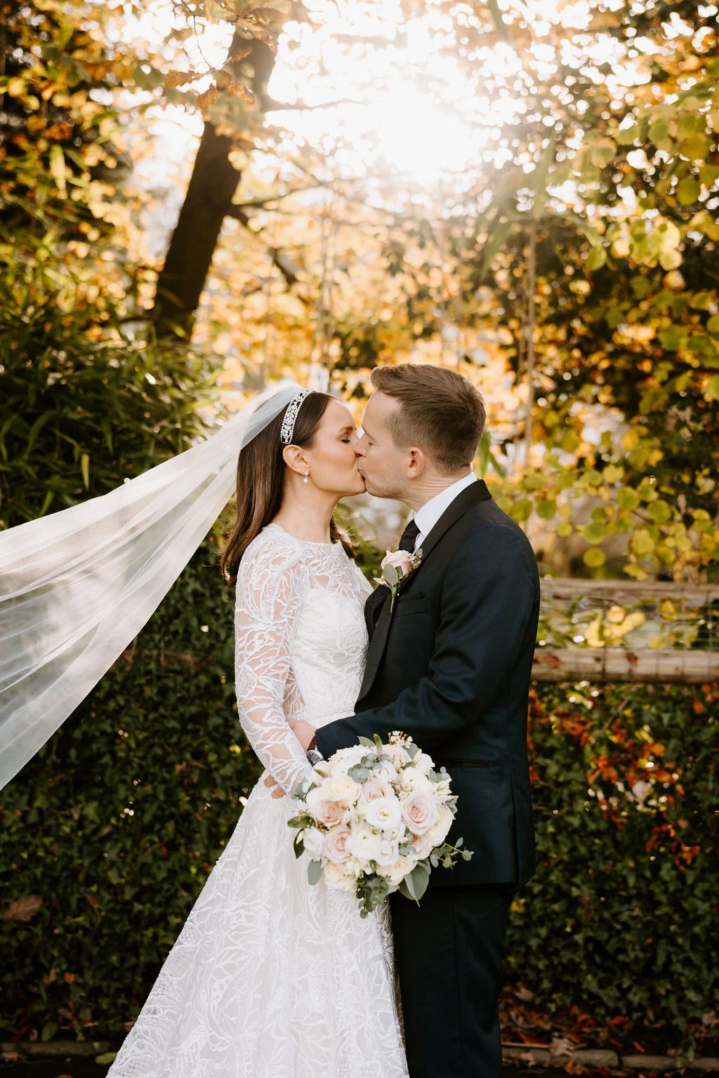Ruth and Rhodri kissing beneath autumn leaves in the sunshine