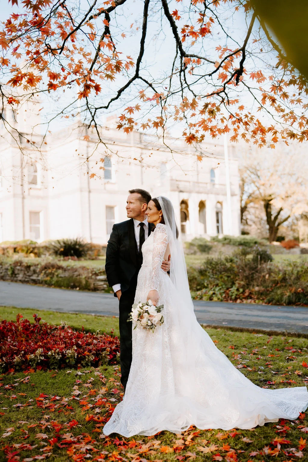 Ruth and Rhodri kissing on a lawn beneath autumn trees