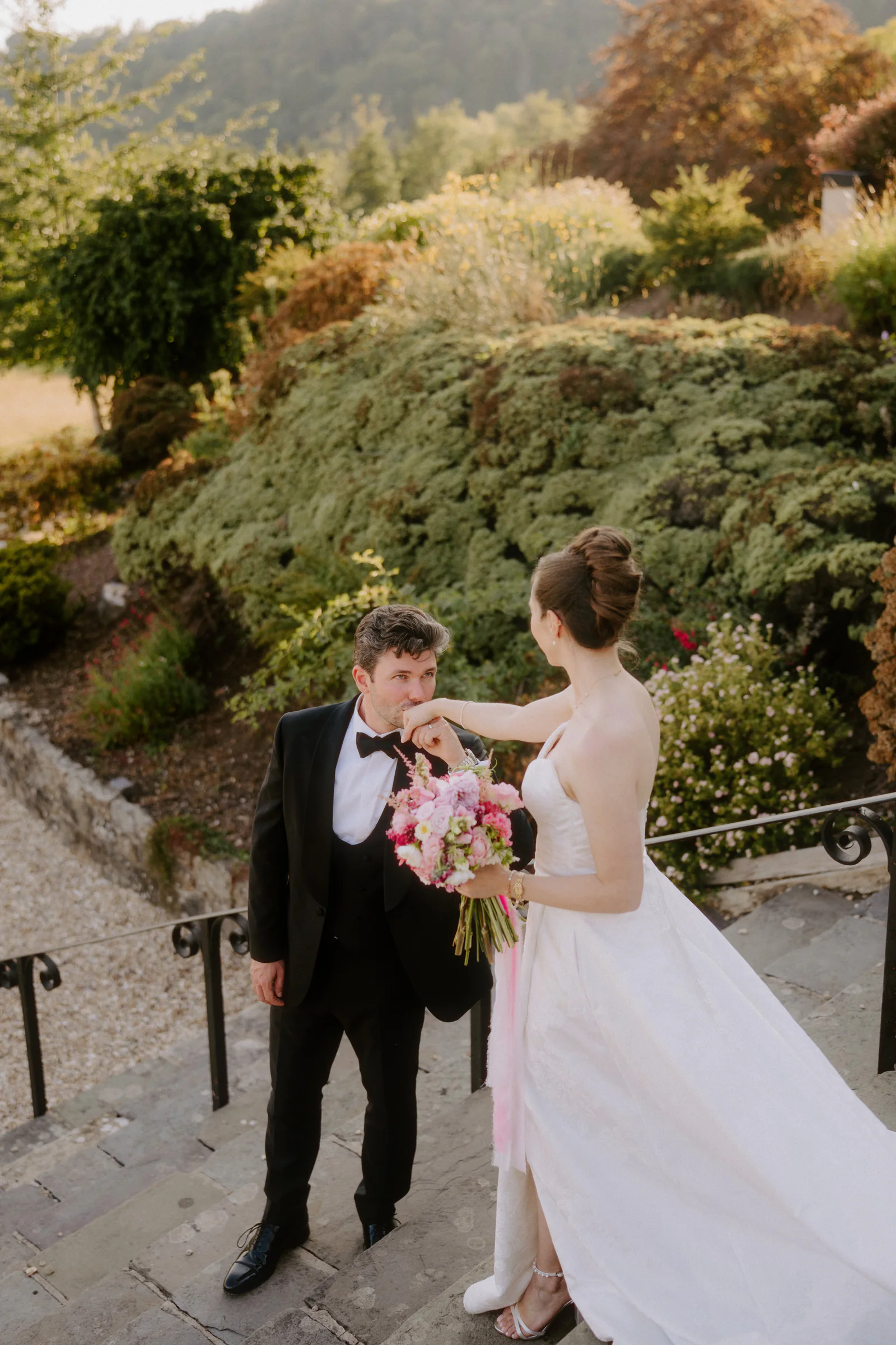 A bride holding her bouquet as her groom kisses her hand in a garden