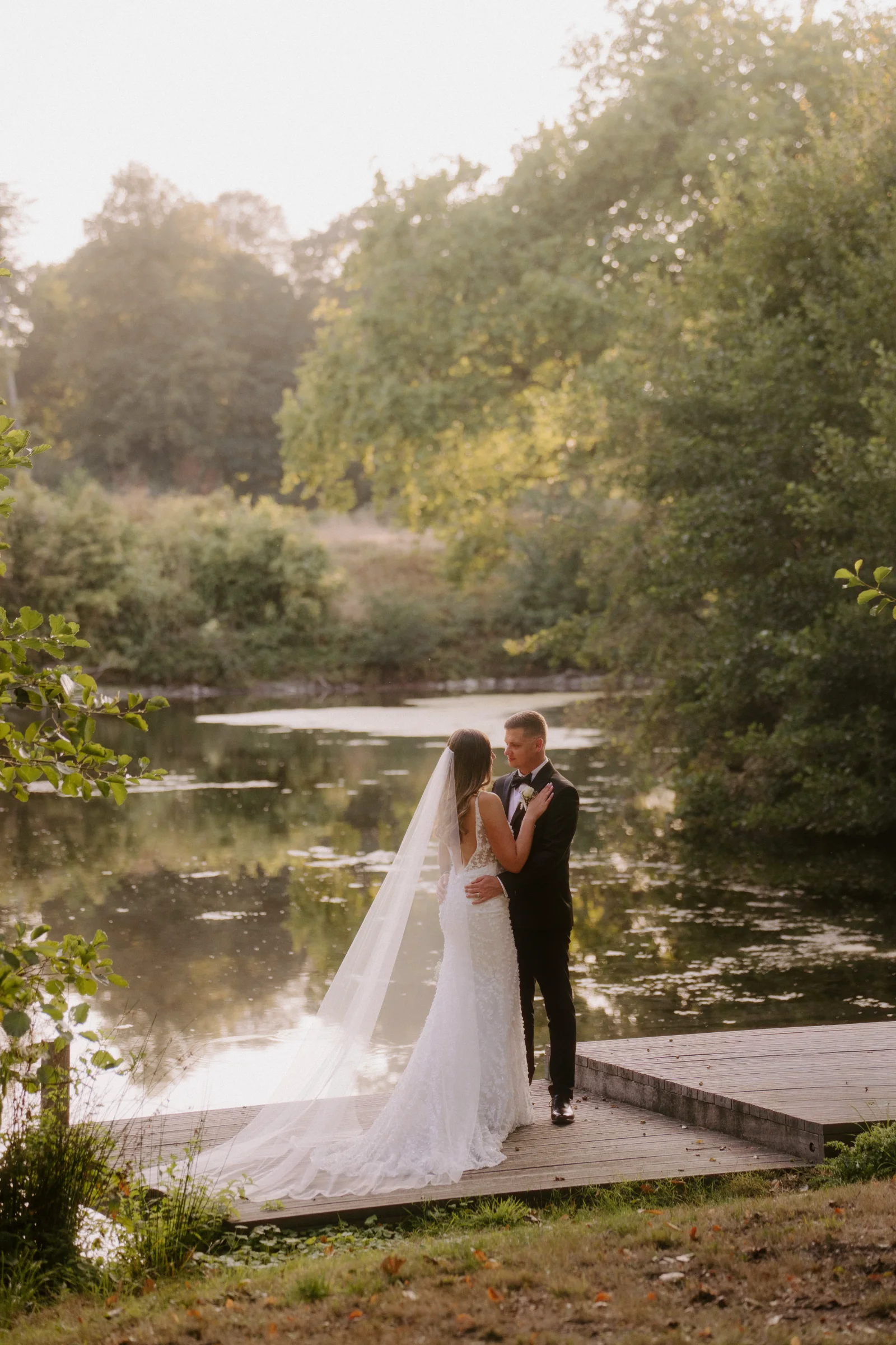 Newlyweds kissing on a wooden dock beside a lake.