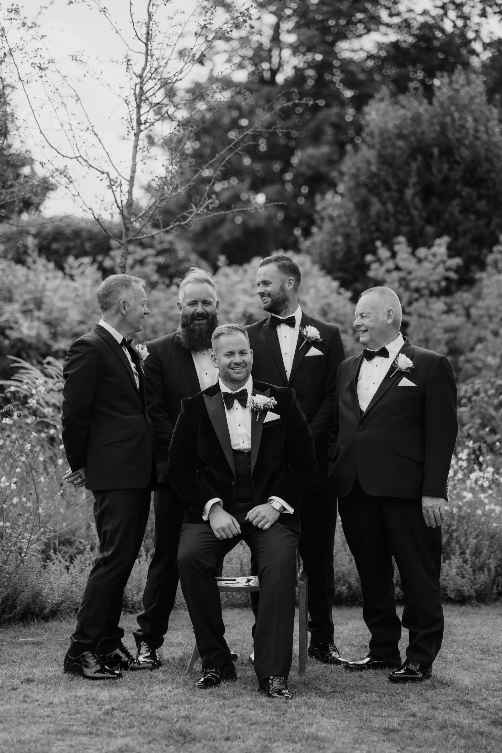 Black and white portrait of a groom with his groomsmen outdoors.