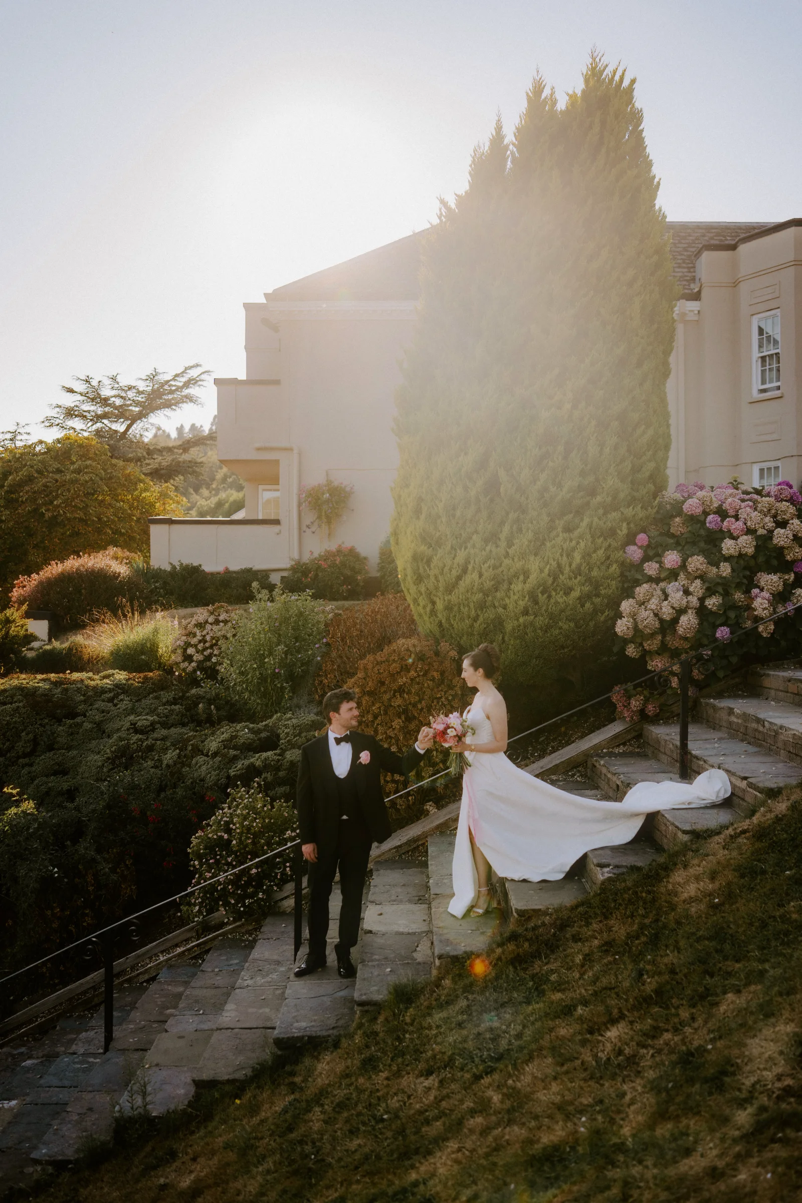 Bride and groom walking together on stone steps outside a country house wedding venue.
