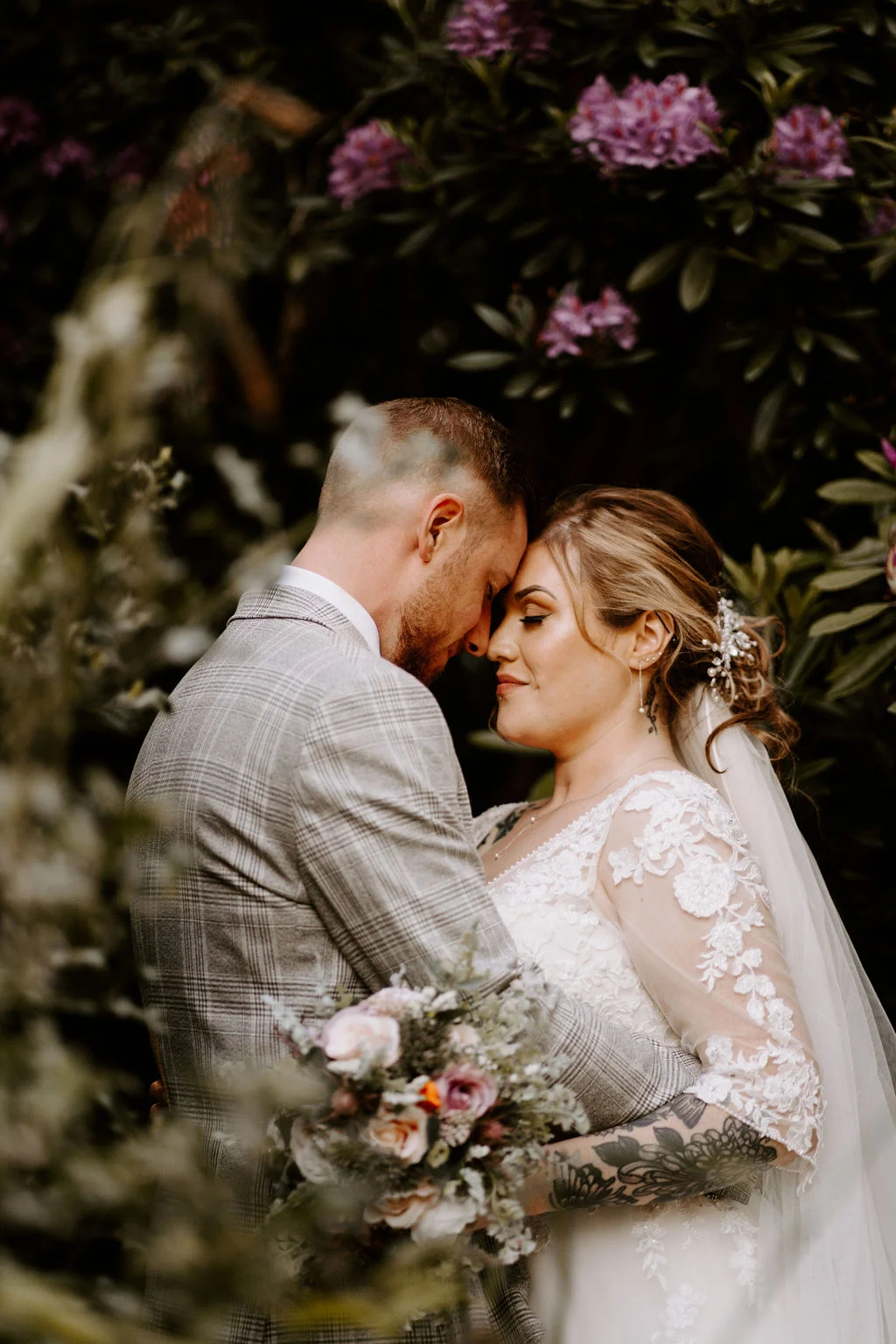 Jess and Matt kissing beneath flowering branches at Kenwood Hall