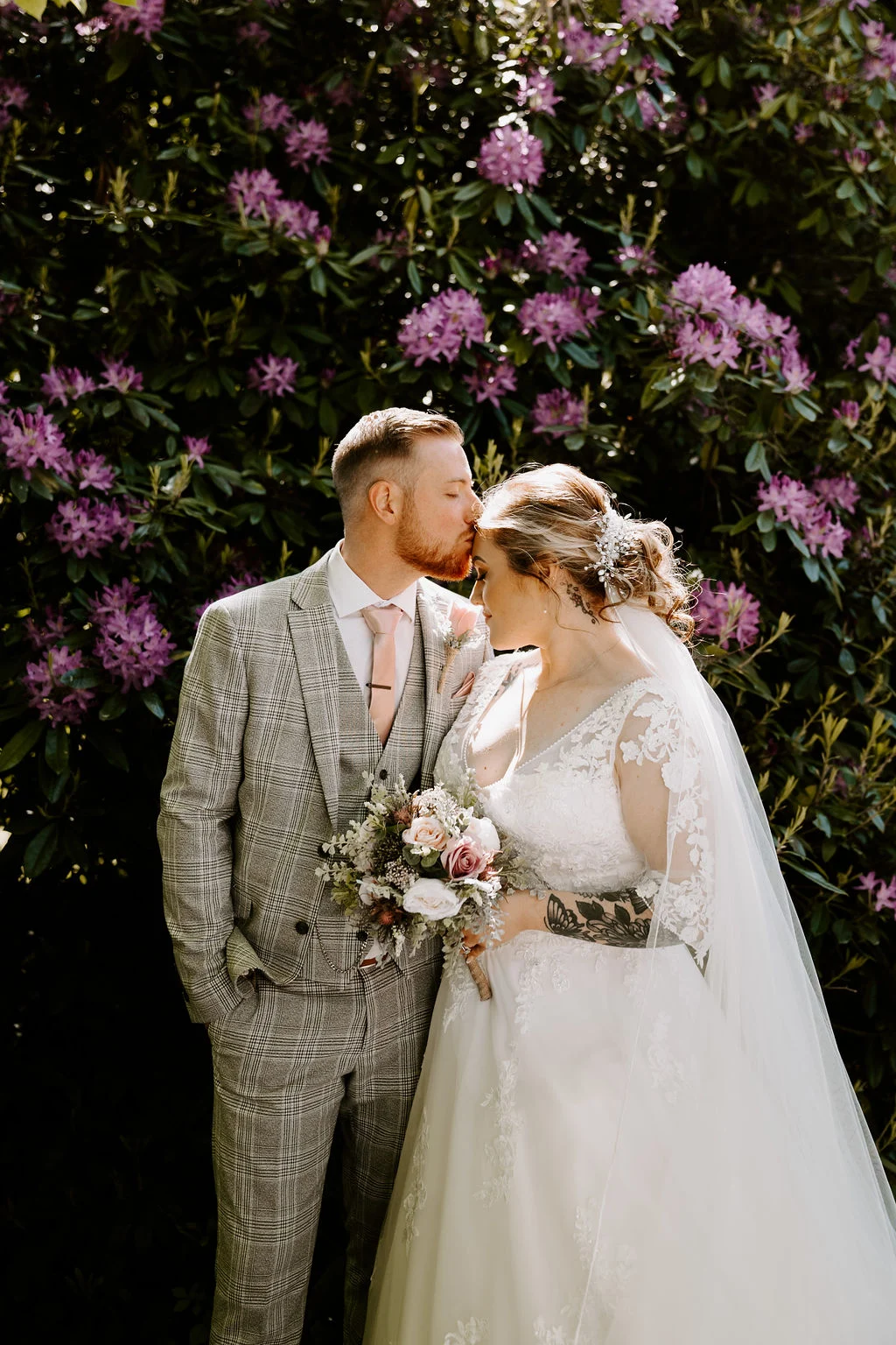 Jess and Matt standing together beneath flowering branches at Kenwood Hall