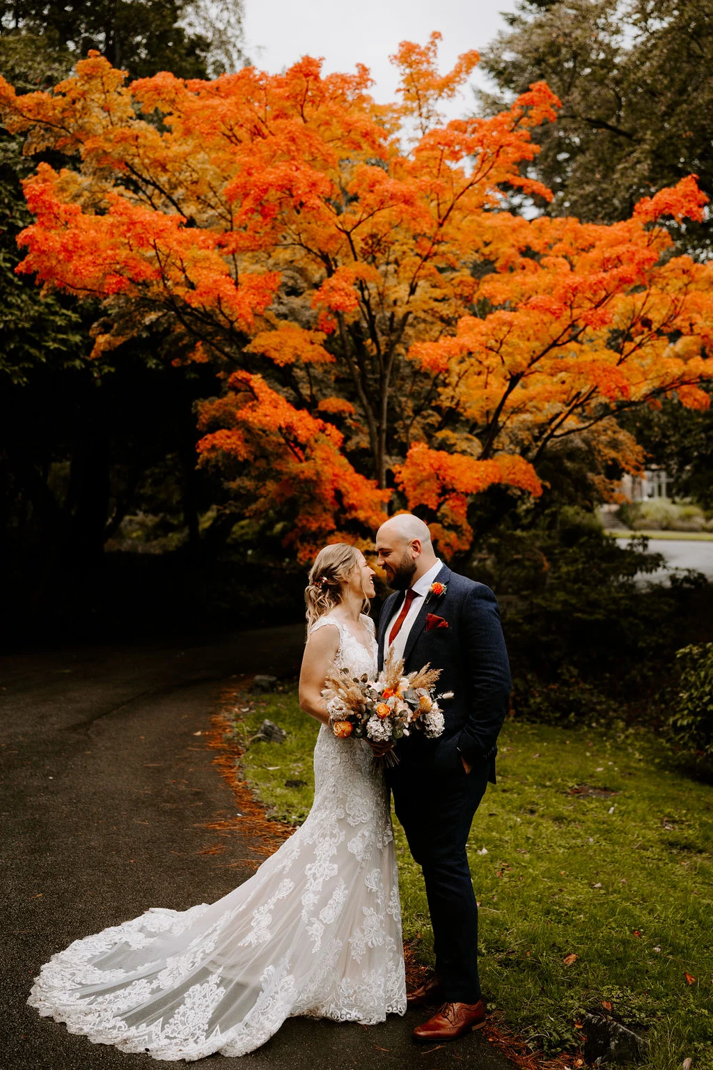 Kirsten and Ben embracing beneath a tree with orange autumn leaves at Whirlow Brook Hall