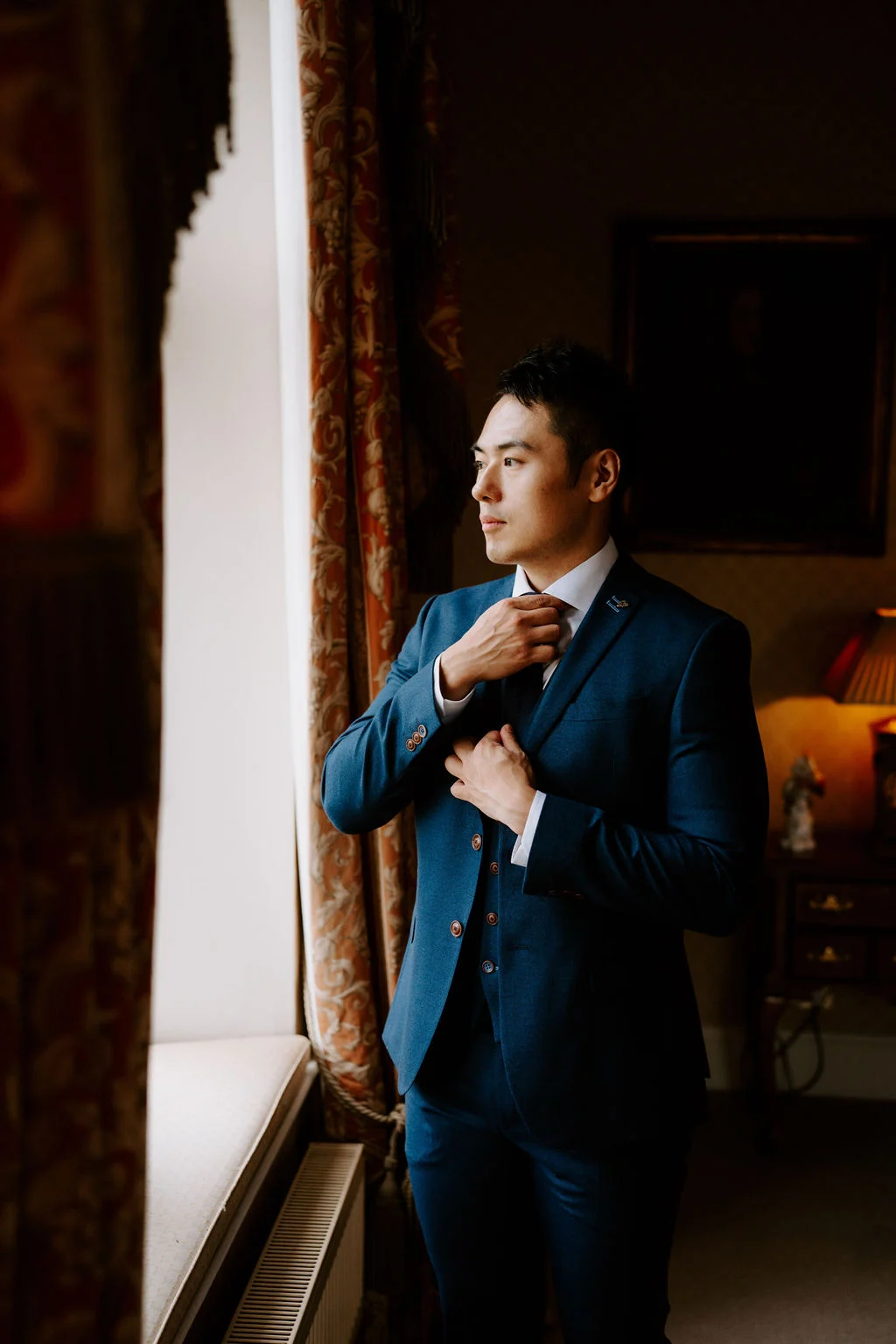 Leslie adjusting his jacket beside a tall window at Carlton Towers