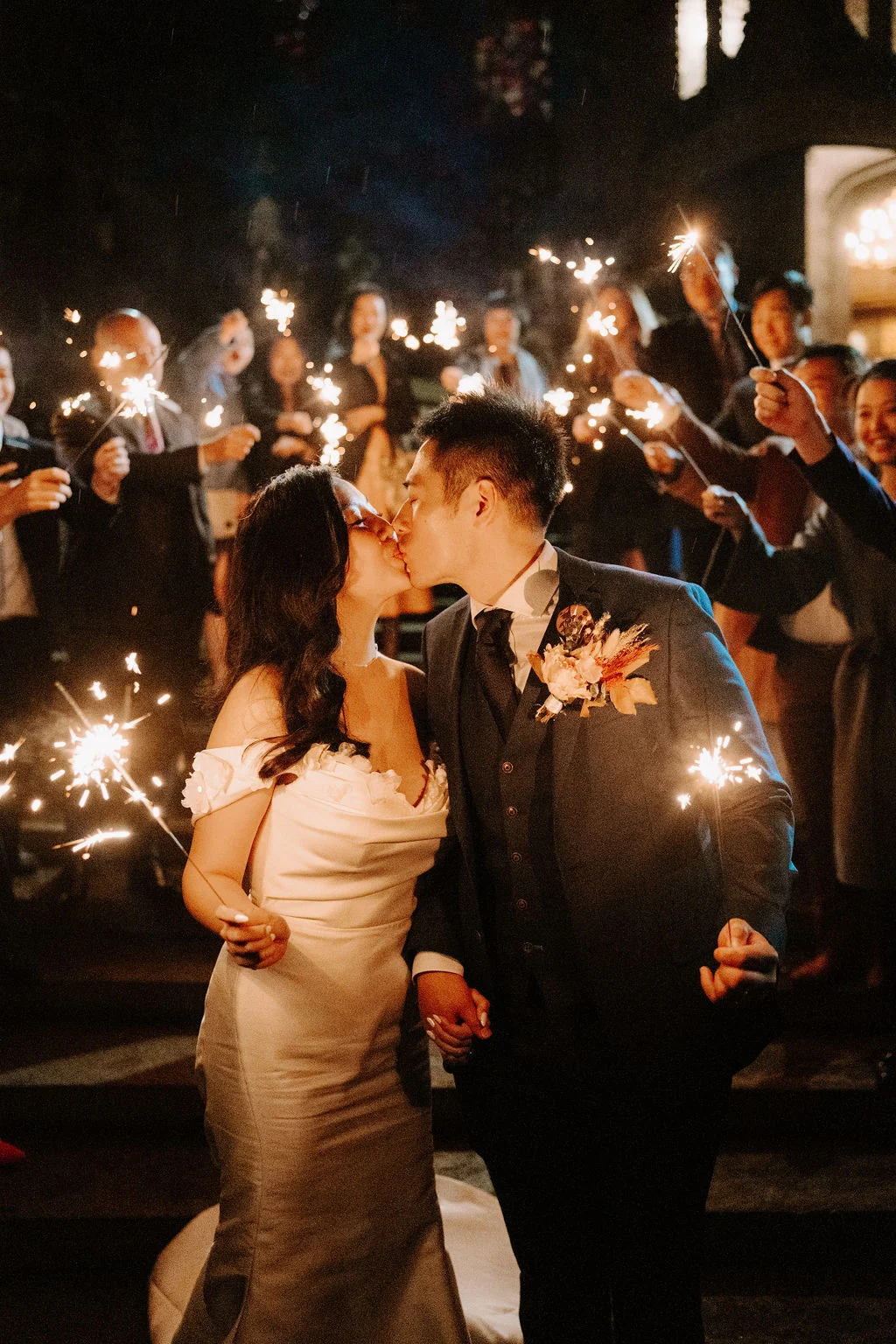 Yukki and Leslie kissing while guests hold sparklers around them
