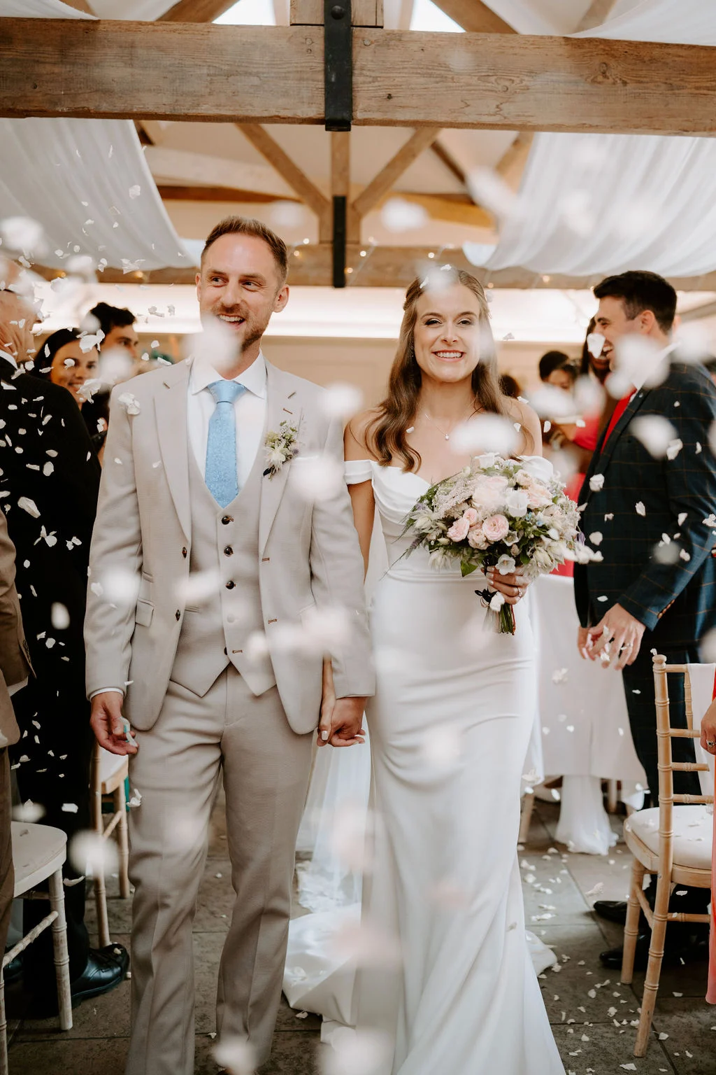 Hannah and Adam walking together through confetti inside the timber barn
