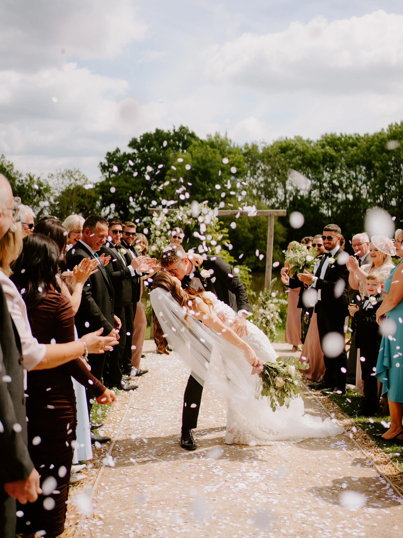 Natalie and Tom kissing beneath confetti at Elmbridge Farm in Worcestershire