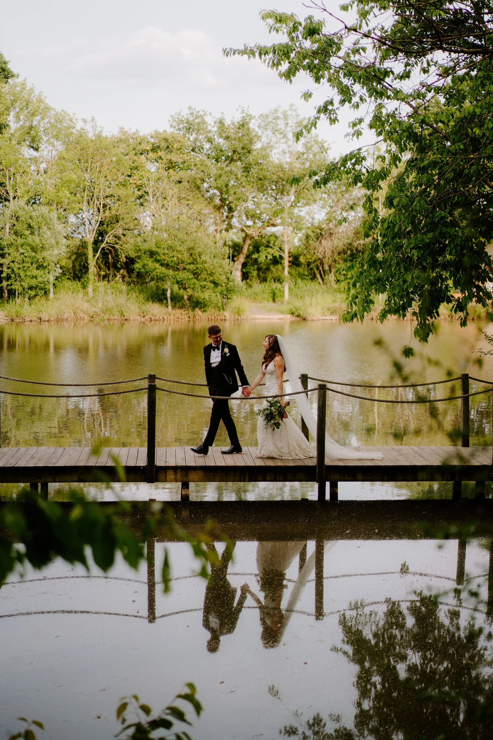 Natalie and Tom on the footbridge reflected in the lake at Elmbridge Farm