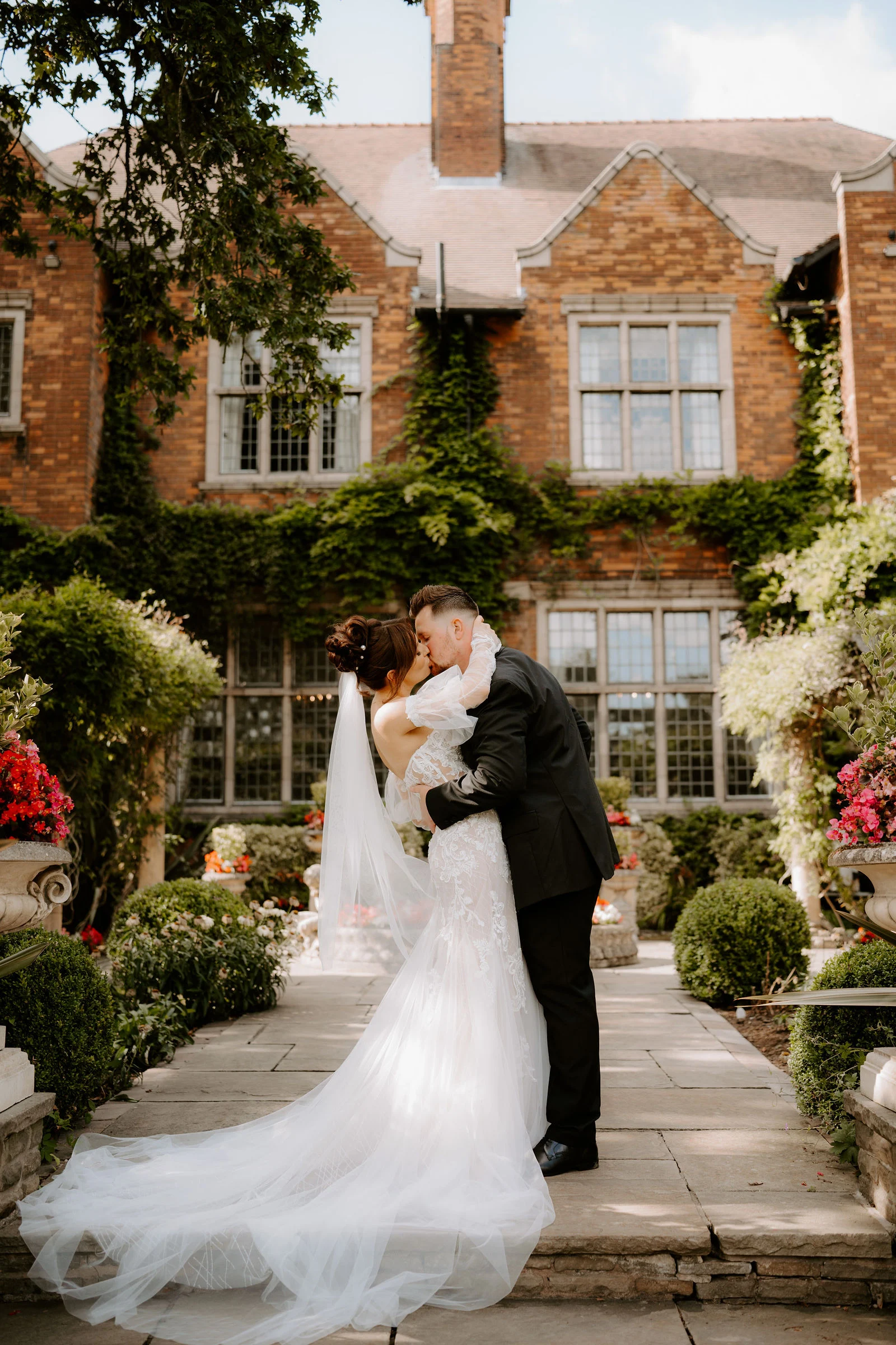 Emily and James kissing in the gardens with Moxhull Hall behind them