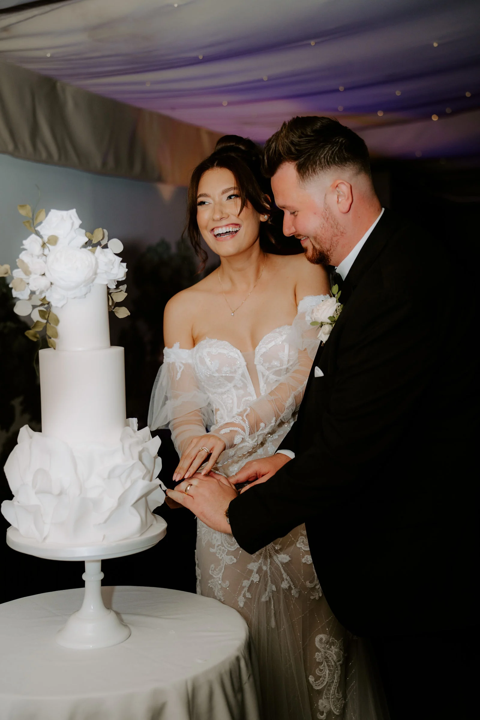 Emily and James laughing together as they cut their wedding cake at Moxhull Hall
