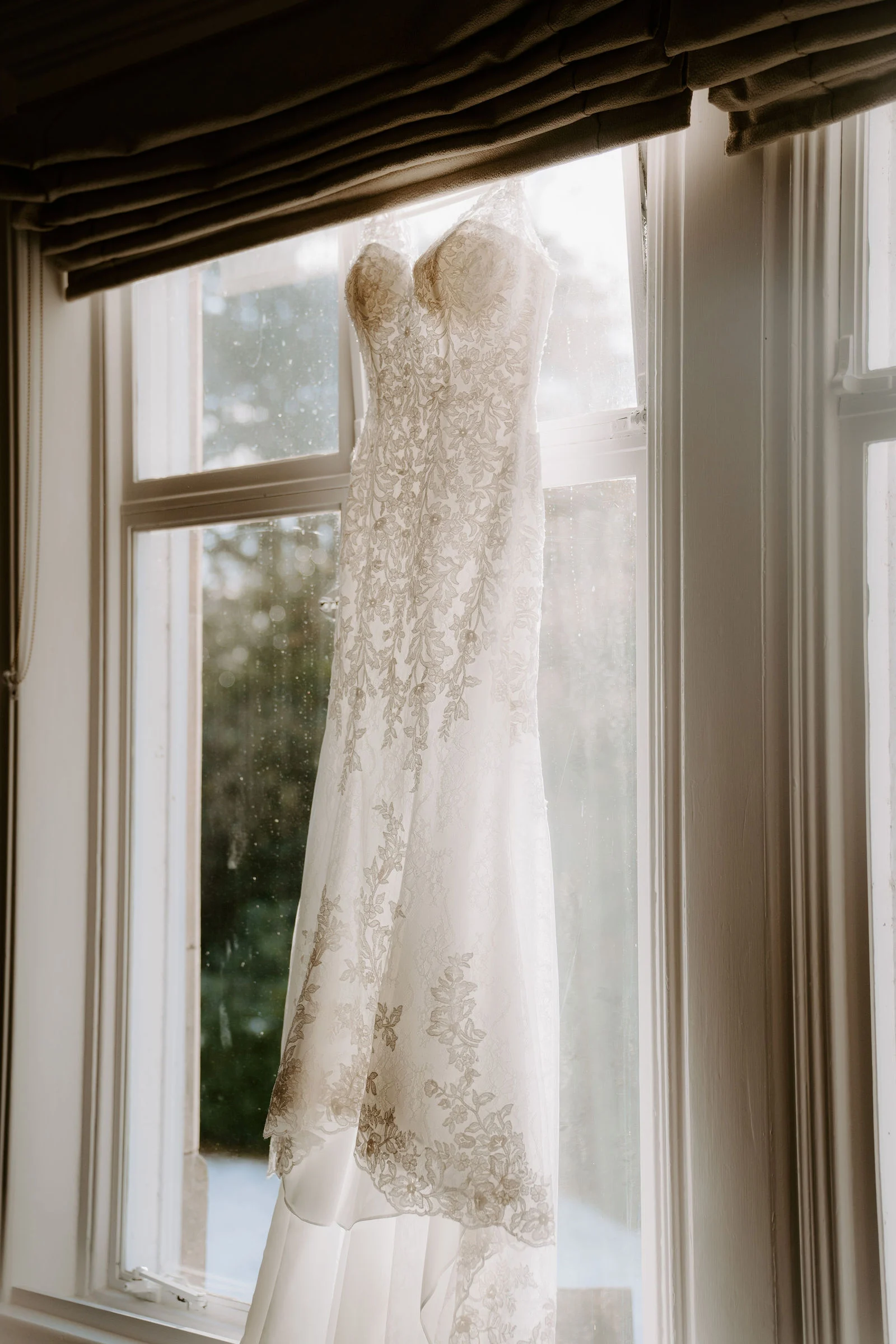 Wedding dress hanging by a window during preparations at Pendrell Hall
