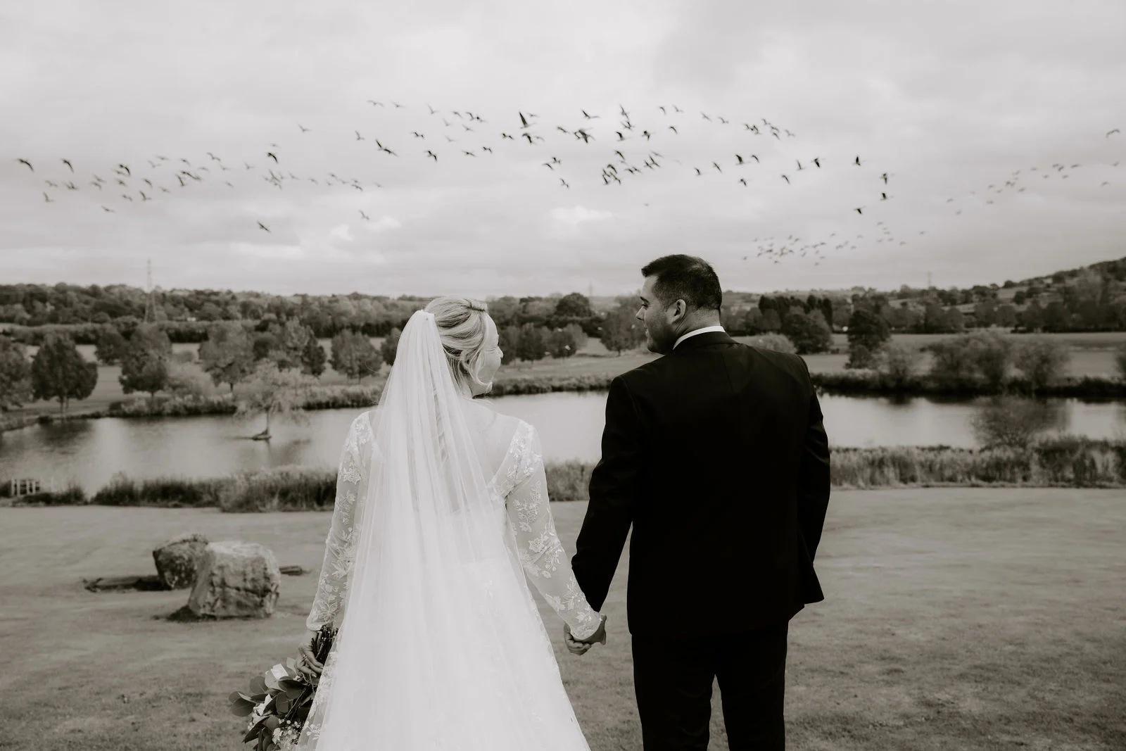 Jolene and Kelvin holding hands above the lake at The Ashes Barns in black and white