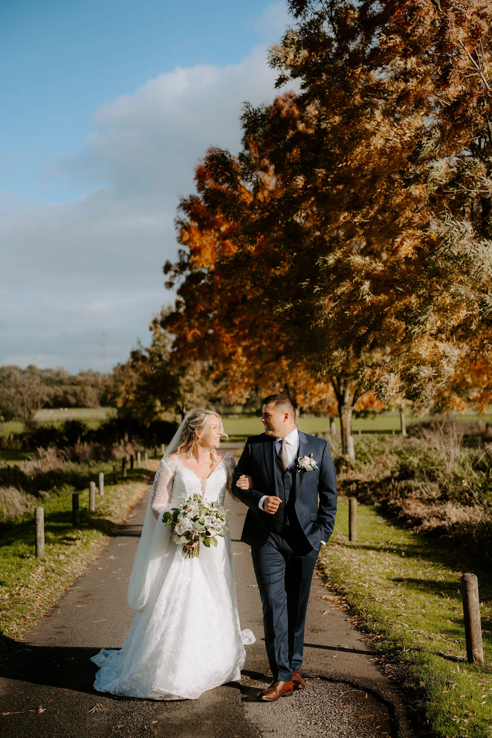 Jolene and Kelvin walking together beside autumn trees at The Ashes Barns
