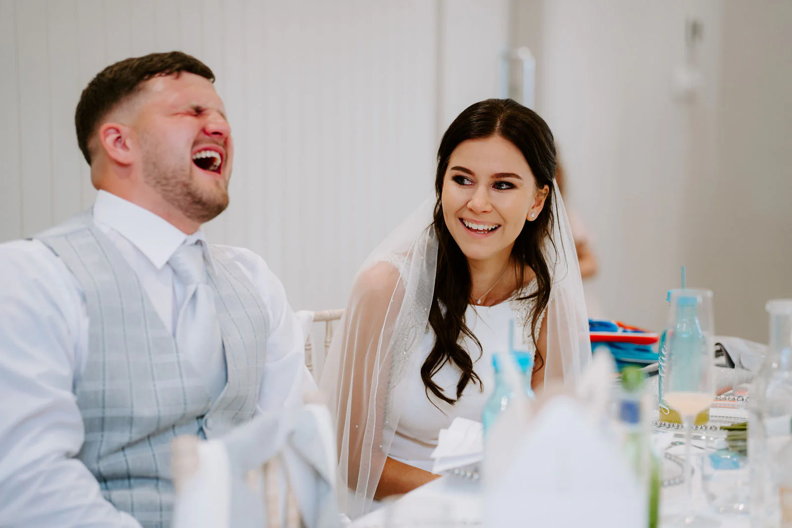 In black and white, Jordan laughs with his eyes shut while Molly in her veil smiles beside him at the top table
