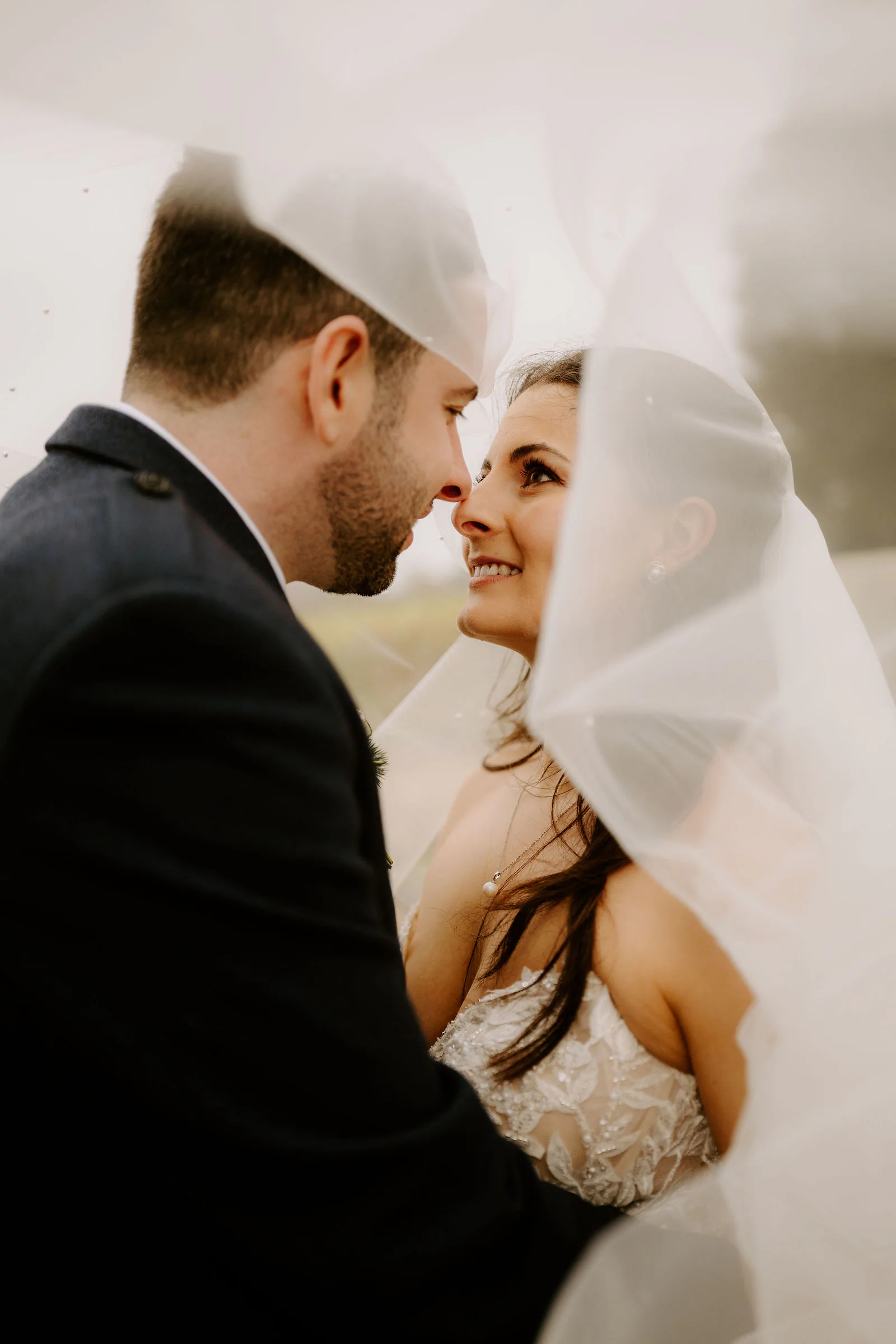 Rose and Ryan share a close, smiling moment beneath her veil, their faces almost touching