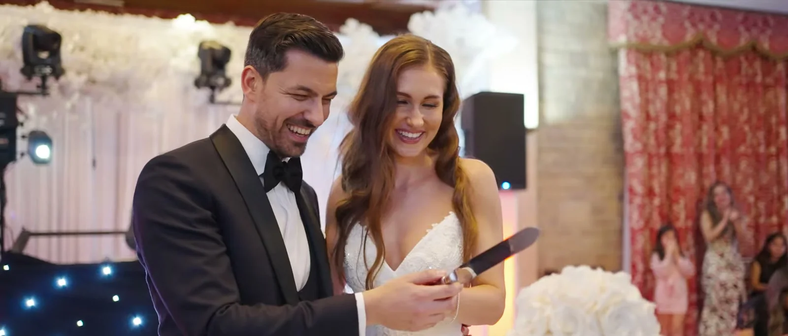 A groom and a bride smile as they cut their wedding cake together