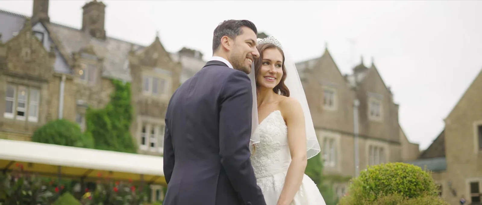 A bride and groom smile together in front of the ivy-covered stone house at South Lodge on a grey day