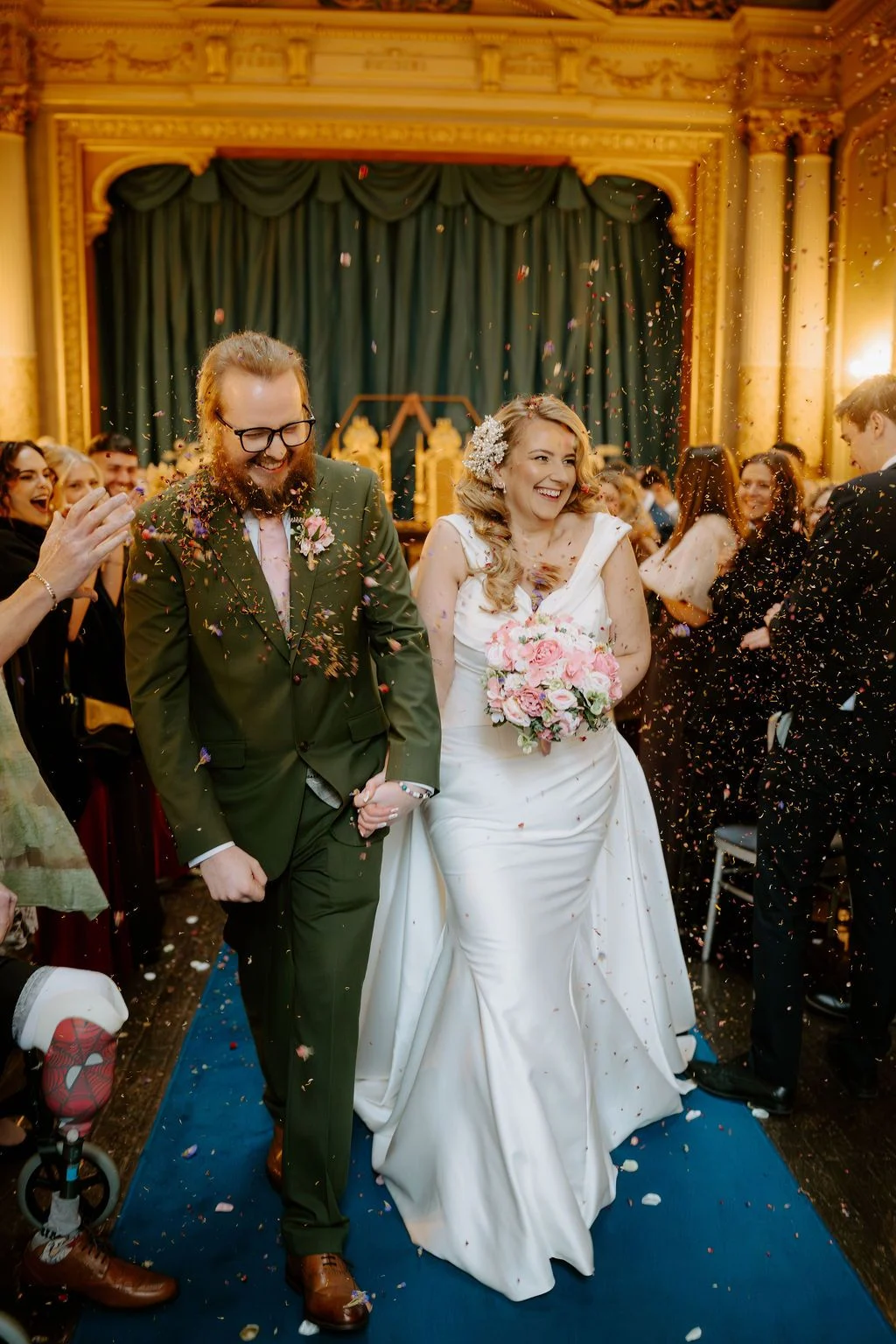 Sophie and Tom walking through confetti in the ornate theatre at Craig y Nos Castle