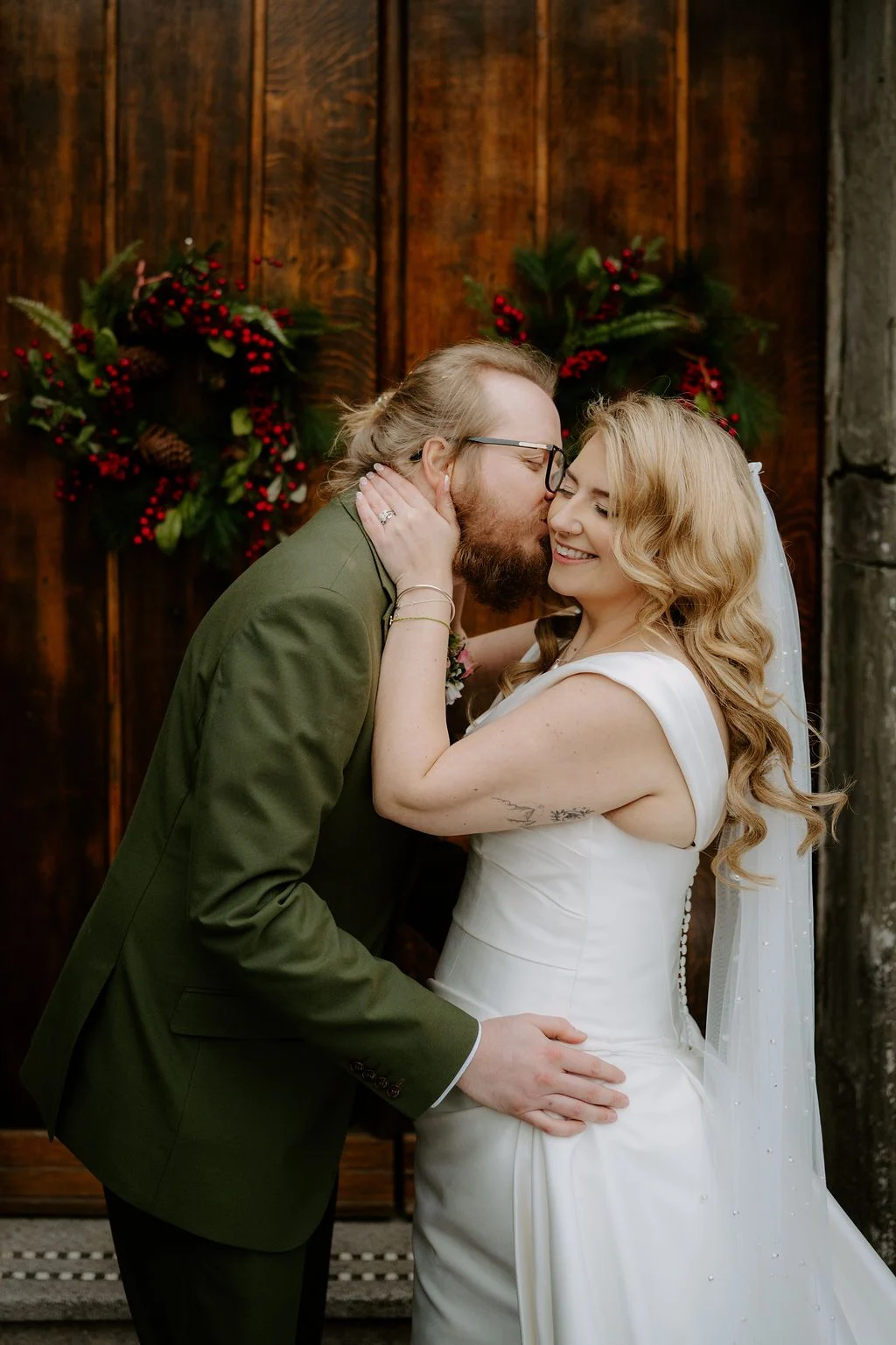Sophie and Tom embracing in front of dark carved wood and flowers