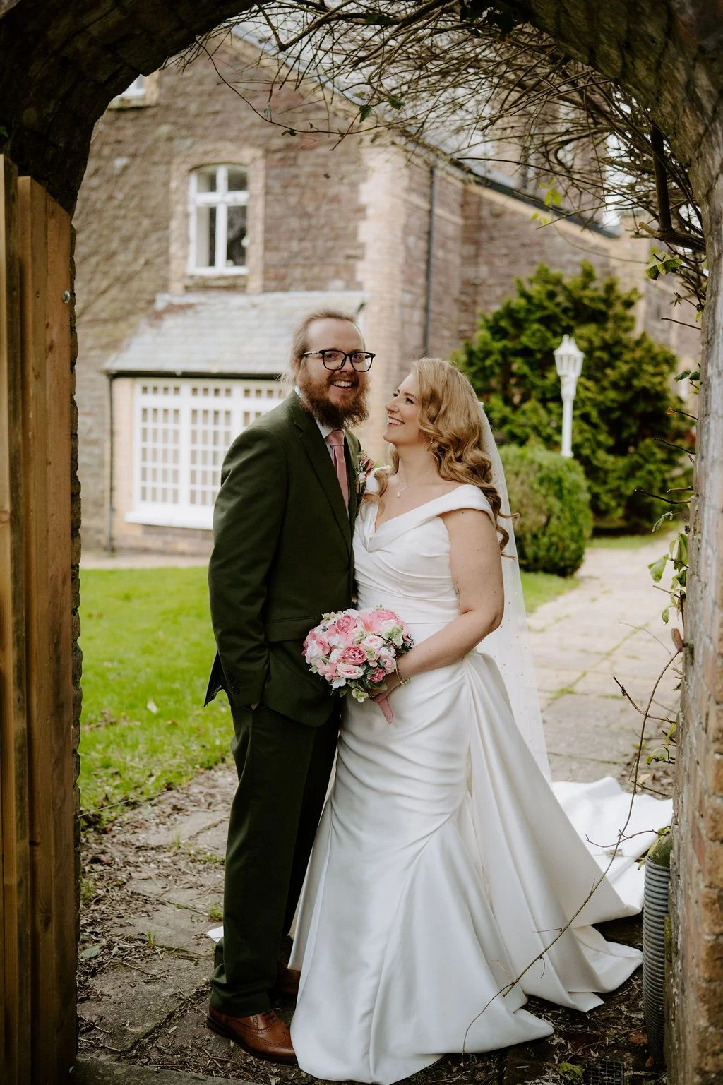 Sophie and Tom standing together on a garden path beneath trees at Craig y Nos